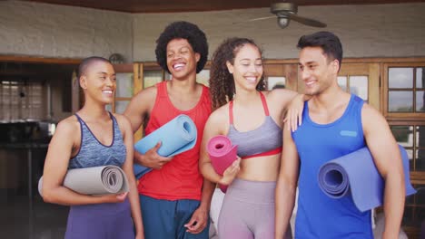 Group-of-diverse-male-and-female-friends-holding-yoga-mats-and-laughing