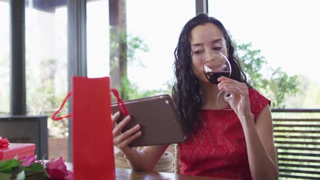 Happy-biracial-woman-making-valentine's-day-video-call-on-tablet,-drinking-wine