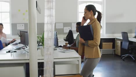 Caucasian-businesswoman-walking-in-office,-holding-documents-and-talking-on-smartphone