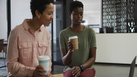 Two-happy-diverse-businesswomen-with-coffee-working-together-in-office