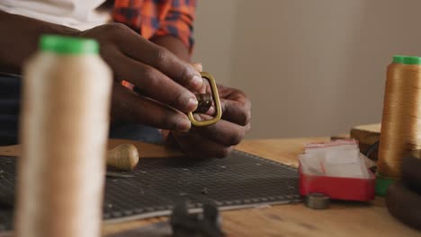 Close-up-of-hands-of-african-american-craftsman-preparing-belt-in-leather-workshop