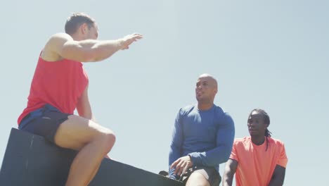 Three-diverse-fit-men-high-fiving-in-the-sun-after-climbing-fence-at-obstacle-course