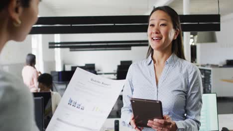 Happy-diverse-businesswomen-holding-documents-and-tablet-and-talking-in-office