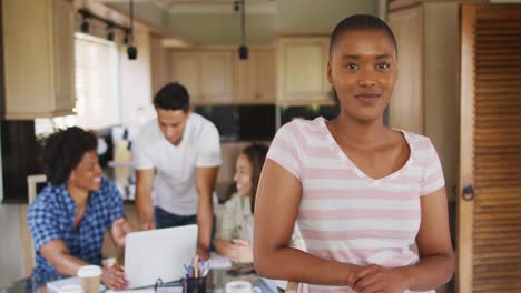 Glückliche-Afroamerikanische-Frau-In-Der-Küche-Mit-Verschiedenen-Freunden,-Die-Im-Hintergrund-Arbeiten