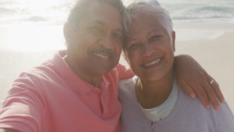 Feliz-Pareja-De-Ancianos-Hispanos-Abrazándose,-Tomándose-Selfie-En-La-Playa-Al-Atardecer