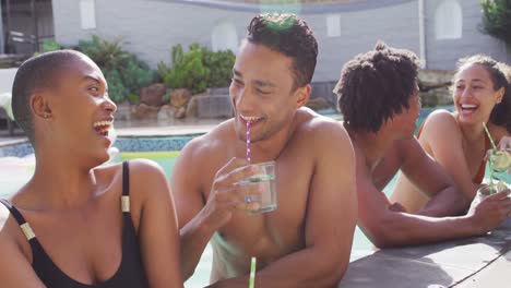 Group-of-diverse-male-and-female-friends-with-drinks-laughing-in-swimming-pool