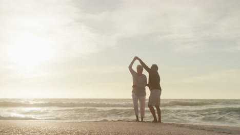 Glückliches-Hispanisches-Seniorenpaar,-Das-Bei-Sonnenuntergang-Am-Strand-Tanzt