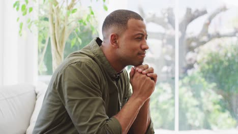 Profile-of-thoughtful-biracial-man-sitting-on-sofa-at-home