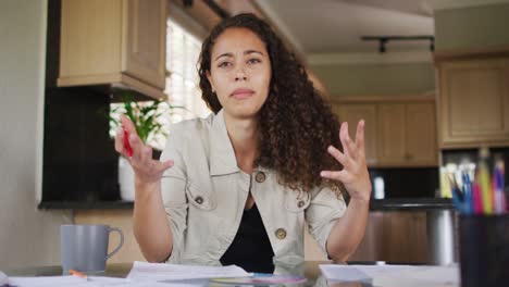 Happy-biracial-woman-gesturing-on-video-call-in-kitchen