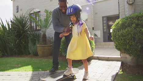 Happy-african-american-father-teaching-daughter-rollerskating-in-front-of-house