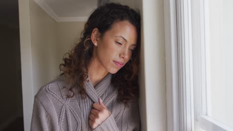 Thoughtful-biracial-woman-standing-at-window-and-looking-into-distance