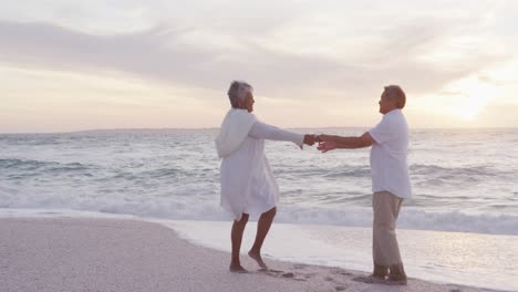 Glückliches-Hispanisches-Frisch-Verheiratetes-älteres-Paar,-Das-Bei-Sonnenuntergang-Am-Strand-Tanzt