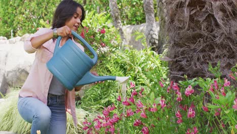 Happy-biracial-woman-gardening,-watering-plants-with-watering-can