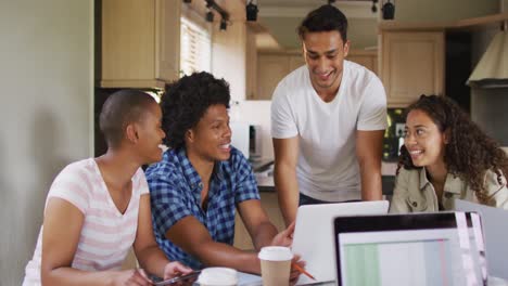 Group-of-diverse-male-and-female-friends-in-kitchen,-laughing-and-working-on-laptops