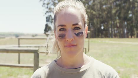 Portrait-of-confident-female-soldier-wearing-eye-black-standing-in-field-on-obstacle-course