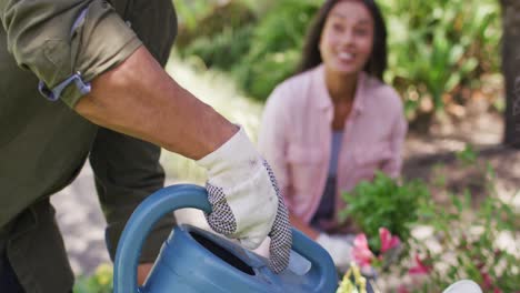 Happy-biracial-woman-gardening,-planting-flower-while-her-partner-watering-plants