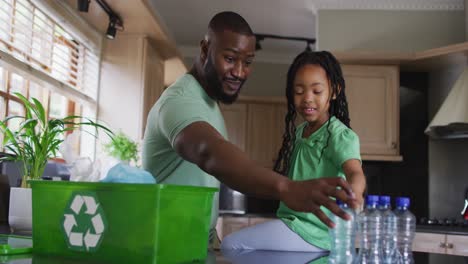 Happy-african-american-father-and-daughter-sorting-plastic-bottles-for-recycling-in-kitchen
