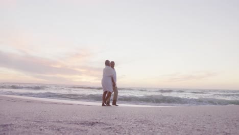 Happy-hispanic-senior-couple-walking-on-beach-at-sunset
