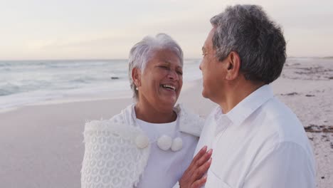 Glückliches-Hispanisches-älteres-Paar,-Das-Sich-Bei-Sonnenuntergang-Am-Strand-Umarmt-Und-Lacht