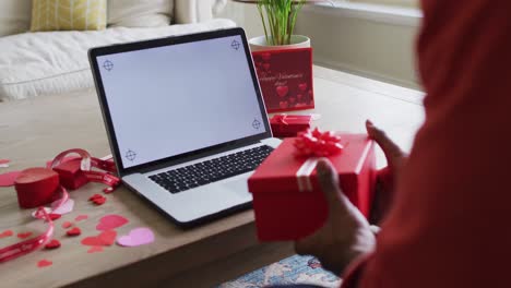Midsection-of-biracial-man-holding-present-and-having-valentine's-video-call-on-laptop