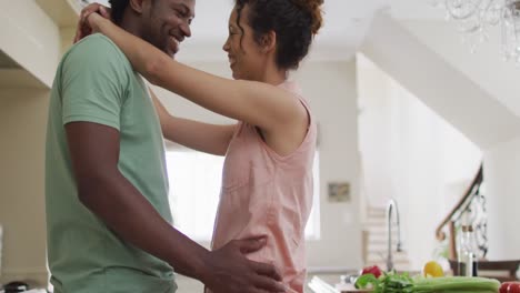 Midsection-of-happy-biracial-couple-hugging-together-in-kitchen