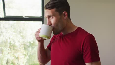 Thoughtful-caucasian-man-is-looking-out-the-window-and-drinking-coffee