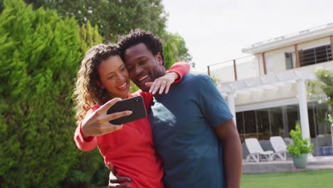 Happy-biracial-couple-taking-selfie-in-garden-after-proposal