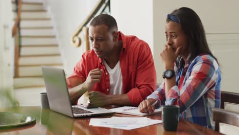 Stressed-biracial-couple-sitting-at-table-with-laptop-and-counting-home-budget