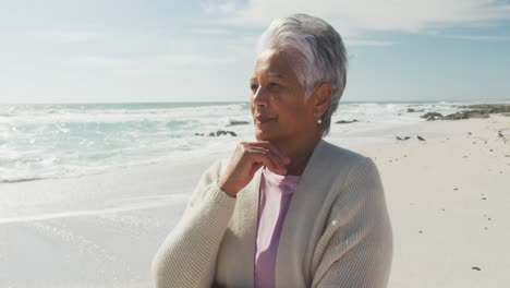 Thoughtful-senior-hispanic-woman-standing-on-beach-and-look-into-distance