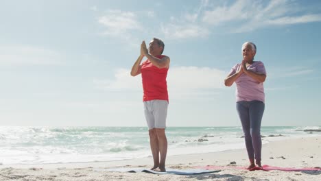 Relaxed-hispanic-senior-couple-practicing-yoga-on-mats-on-beach