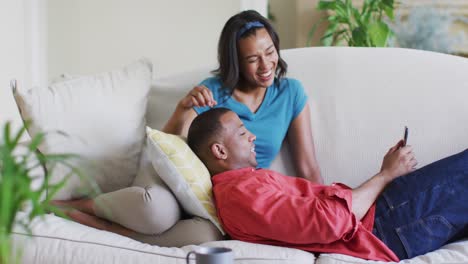 Happy-biracial-couple-on-sofa-with-smartphone-and-talking