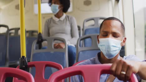 African-american-man-and-woman-with-face-masks-sitting-in-bus