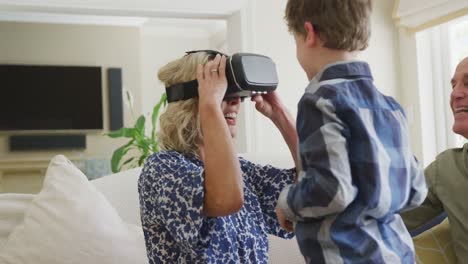 Happy-senior-caucasian-couple-with-grandson-using-vr-headset-in-living-room
