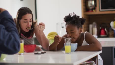 Happy-caucasian-lesbian-couple-and-their-african-american-daughter-eating-breakfast-in-kitchen