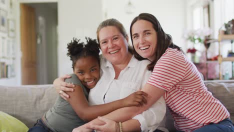 Portrait-of-happy-caucasian-lesbian-couple-and-their-african-american-daughter-embracing-and-smiling