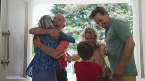 Happy-caucasian-couple-with-son-opening-door-and-greeting-their-grandparents