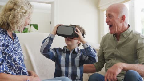 Glückliches-älteres-Kaukasisches-Paar-Mit-Enkel,-Der-Im-Wohnzimmer-Ein-VR-Headset-Verwendet
