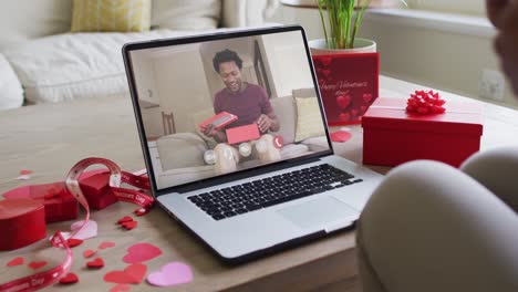 Fröhlicher-Afroamerikanischer-Mann,-Der-Ein-Geschenk-öffnet-Und-Einen-Videoanruf-Zum-Valentinstag-Auf-Dem-Laptop-Tätigt