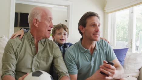 Happy-caucasian-grandfather-and-adult-son-with-grandson-watching-tv-and-supporting-in-living-room