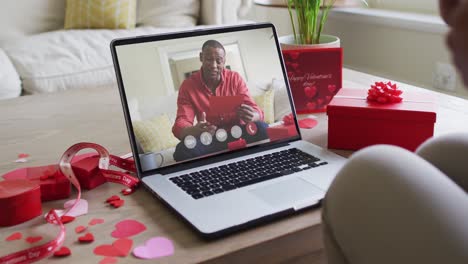 Fröhlicher-Afroamerikanischer-Mann,-Der-Ein-Geschenk-öffnet-Und-Einen-Videoanruf-Zum-Valentinstag-Auf-Dem-Laptop-Tätigt