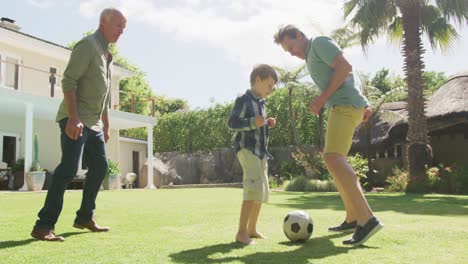 Glücklicher-Kaukasischer-Großvater-Mit-Erwachsenem-Sohn-Und-Enkel,-Der-Im-Garten-Fußball-Spielt