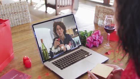 Biracial-man-with-champagne-making-valentine's-day-video-call-on-laptop