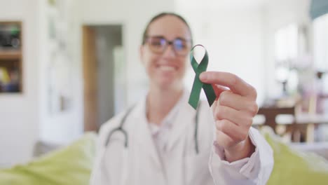 Portrait-of-happy-caucasian-female-doctor-holding-green-awareness-ribbon