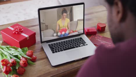 Happy-biracial-woman-opening-gift-and-making-valentine's-day-video-call-on-laptop