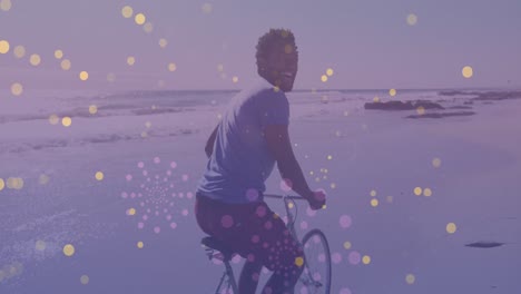 Yellow-spots-of-light-against-portrait-of-african-american-man-riding-a-bicycle-at-the-beach