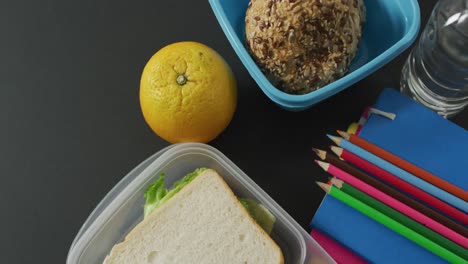 Video-of-healthy-packed-lunch-of-fruit-and-vegetables,-with-coloured-pencils-on-schoolbag