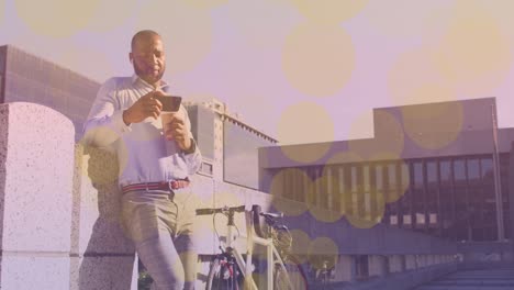 Yellow-spots-of-light-floating-against-african-american-man-with-a-bicycle-using-smartphone