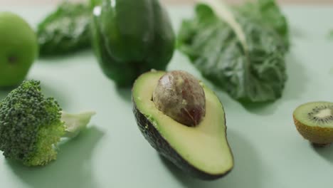 Video-of-fresh-avocado,-broccoli,-green-pepper-and-green-leaves-on-green-background