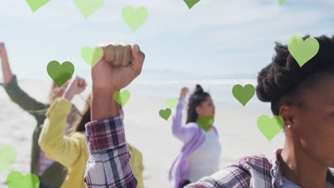 Multiple-green-hearts-floating-against-group-of-diverse-people-protesting-at-the-beach