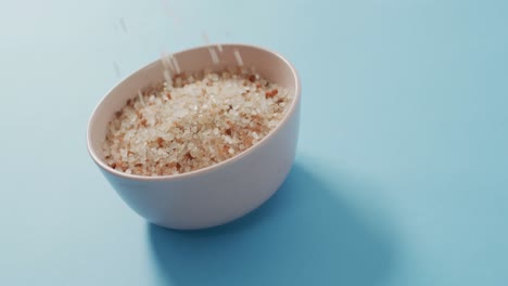 Video-of-close-up-of-bowl-of-organic-salt-on-blue-background